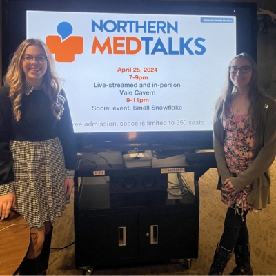 Both Kaylie and Nicole standing in front of screen with MedTalks slide