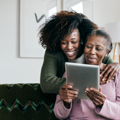 A young girl watching her senior mother interact with Crohn's and Colitis Connect from a tablet device