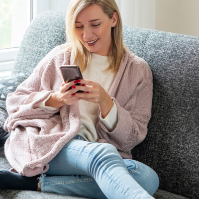 A young woman sitting on a couch looking at Peer Support on her phone